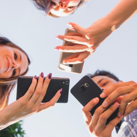 tri mlade osobe gledaju u mobitel slikano odozdo