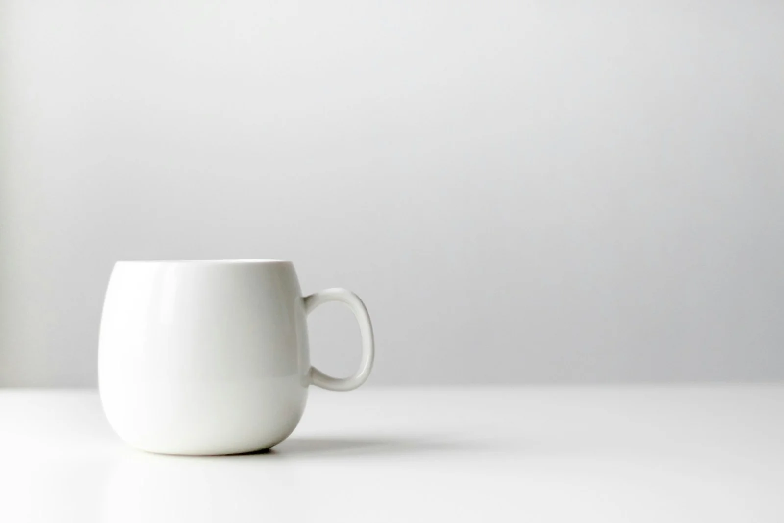 Stack of cream ceramic mugs in soft daylight on a wooden surface