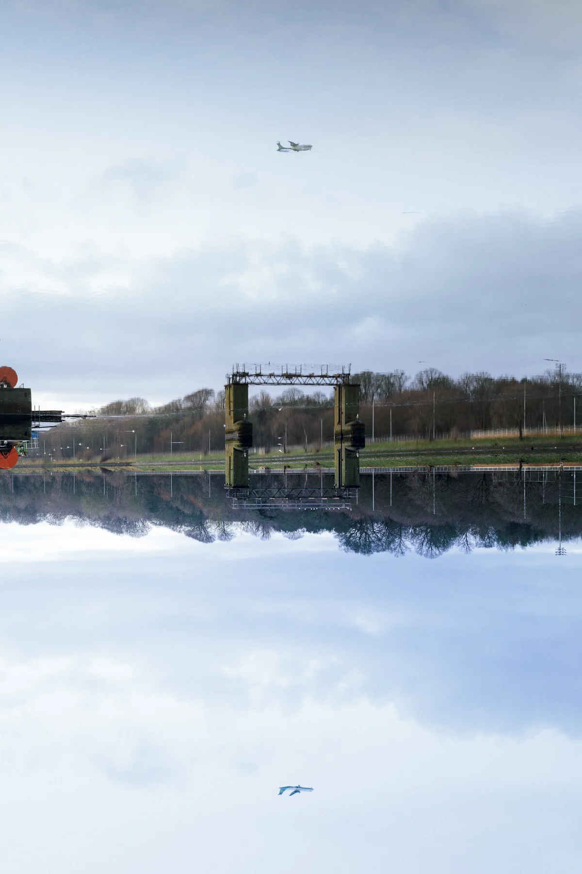 A symmetrical reflection of a landscape with trees and a structure in a still body of water.