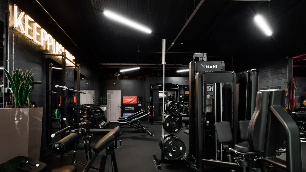 A moody gym interior featuring a bright neon 'KEEP PUSHING' sign and various weightlifting machines.