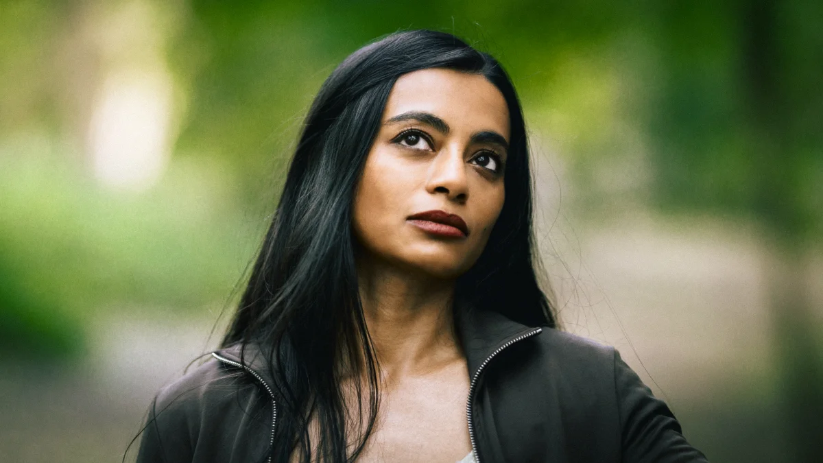 Close-up portrait of a woman with long dark hair looking thoughtfully against a blurred green background