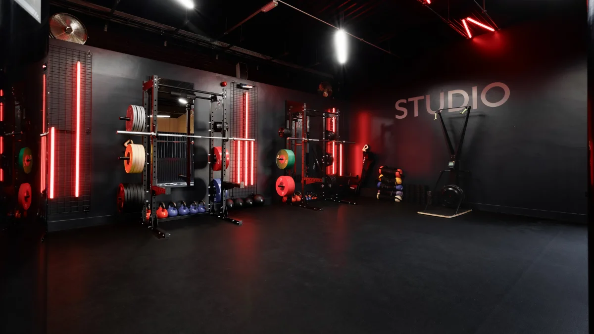 A dark, cinematic gym studio featuring red neon lights, weightlifting racks, and kettlebells.
