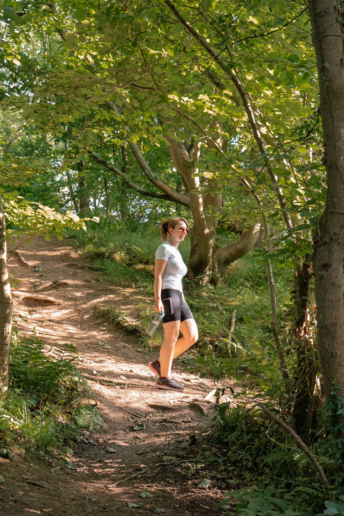 A woman in athletic wear walking along a sunlit forest path.