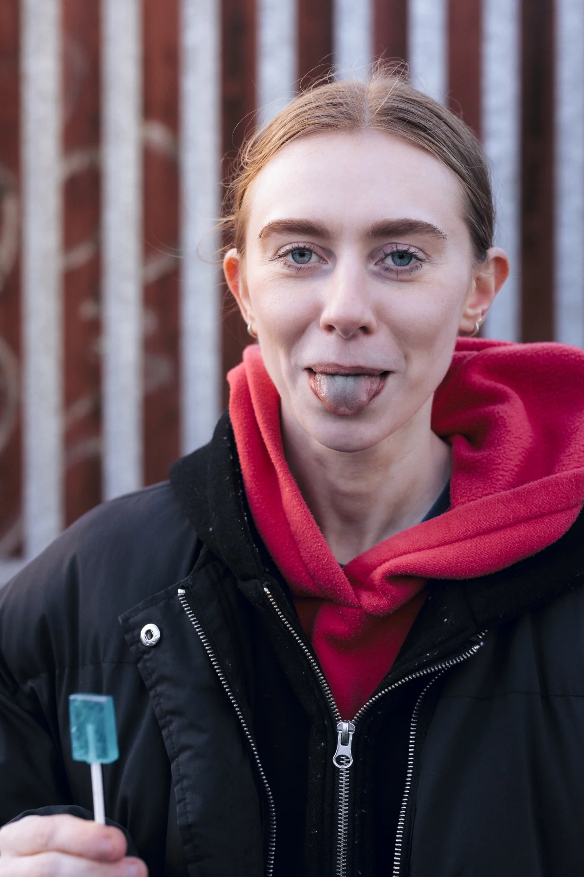 Close-up portrait of a woman sticking her tongue out while holding a blue popsicle outdoors.