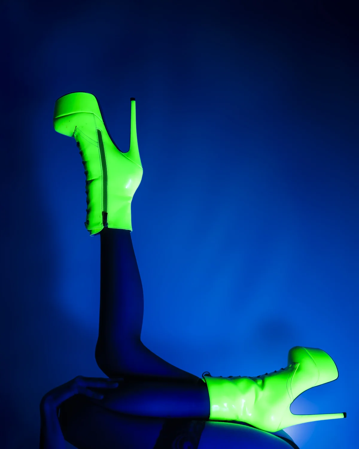 Neon green high-heeled boots against a dark blue background.