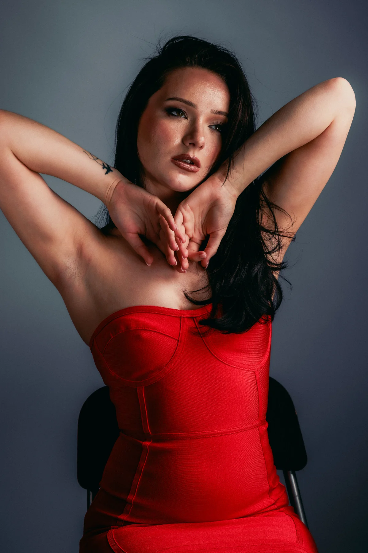 A woman with long dark hair wearing a red strapless dress, posing in a studio.