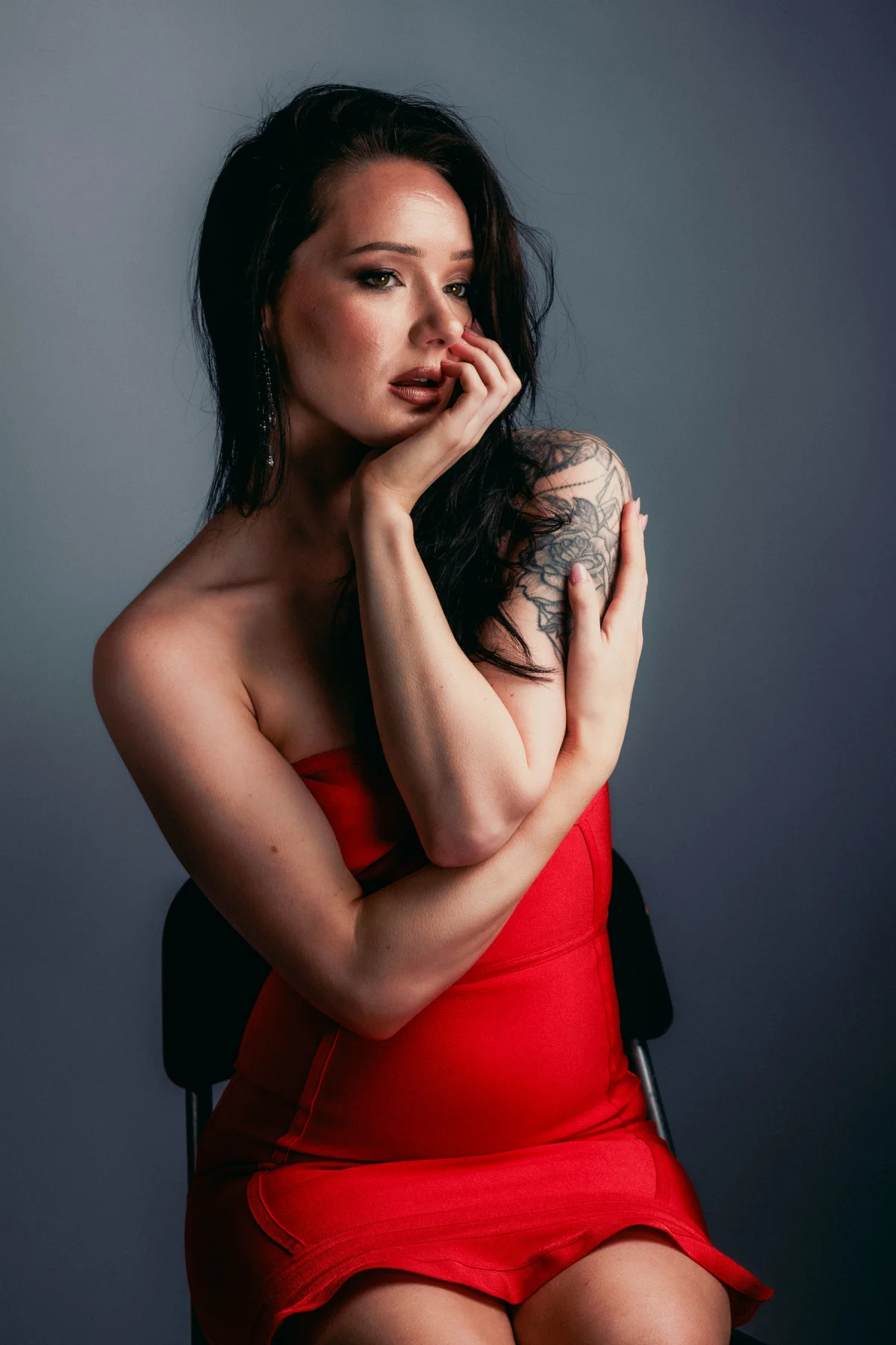 A woman in a red strapless dress posing against a grey studio background.