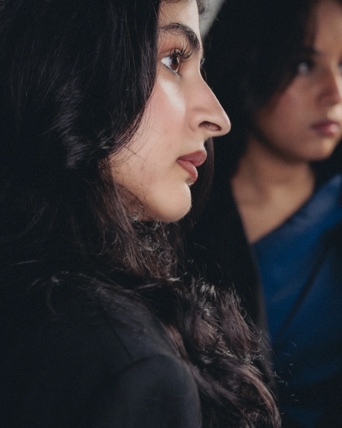 Side profile portrait of a young woman with dark hair and a thoughtful expression, featuring her reflection.