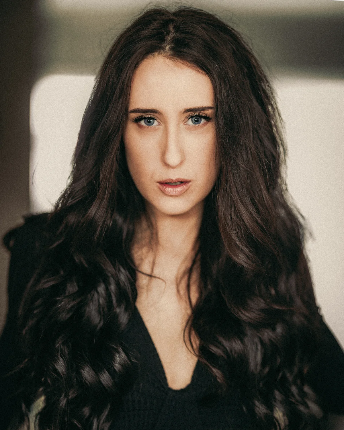 Close-up portrait of a woman with long wavy dark brown hair and blue eyes looking at the camera.
