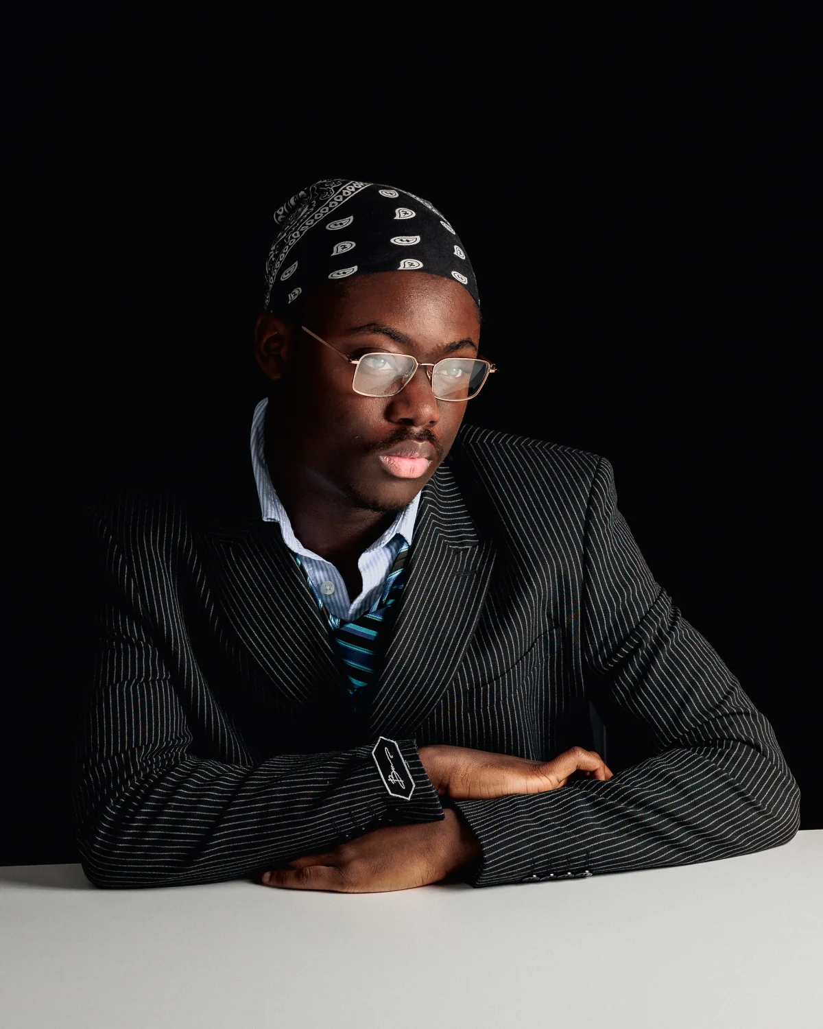 A young man in a pinstripe suit and black bandana posing against a dark background.