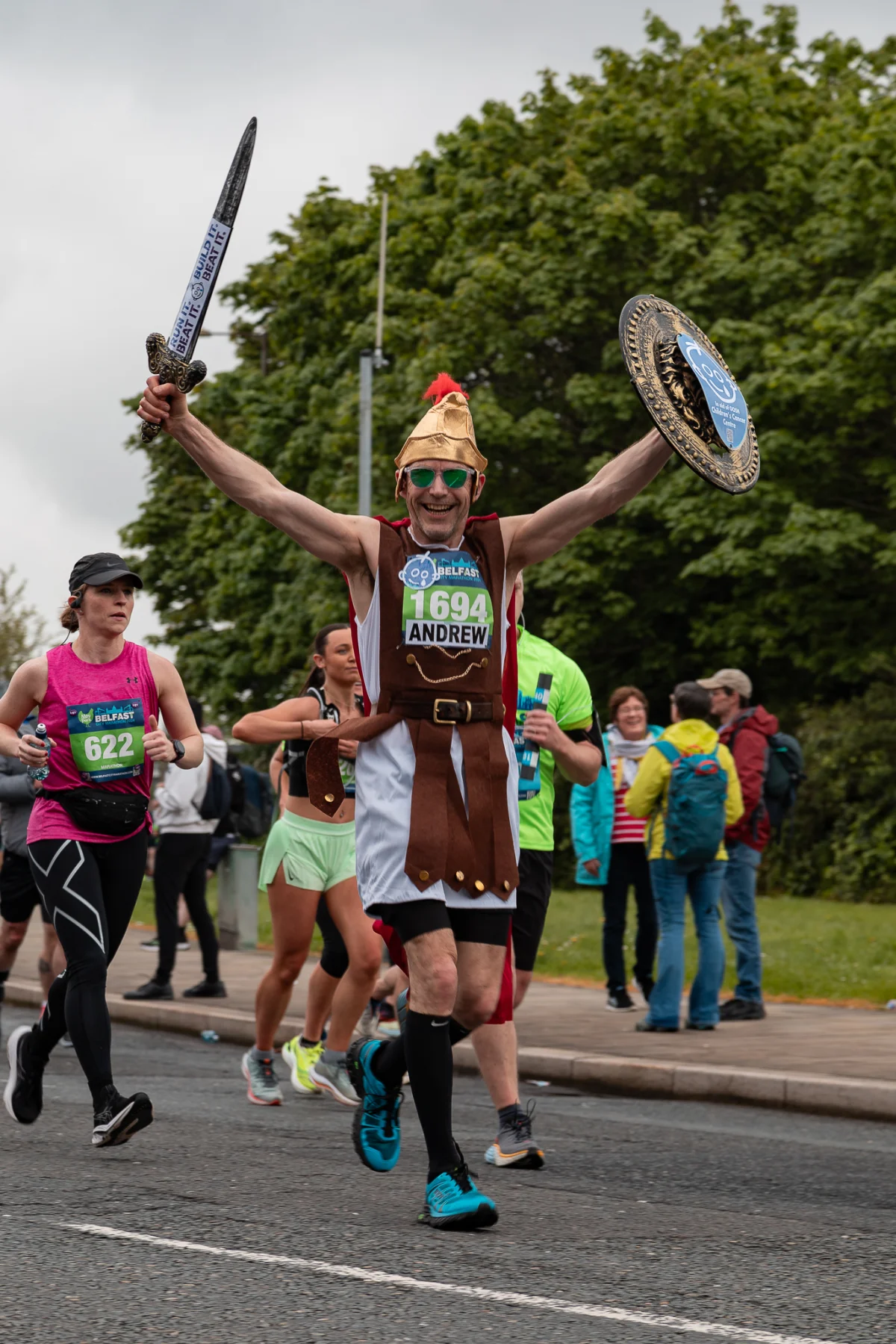 A man in a Roman soldier costume celebrates during a race, holding a sword and shield aloft.