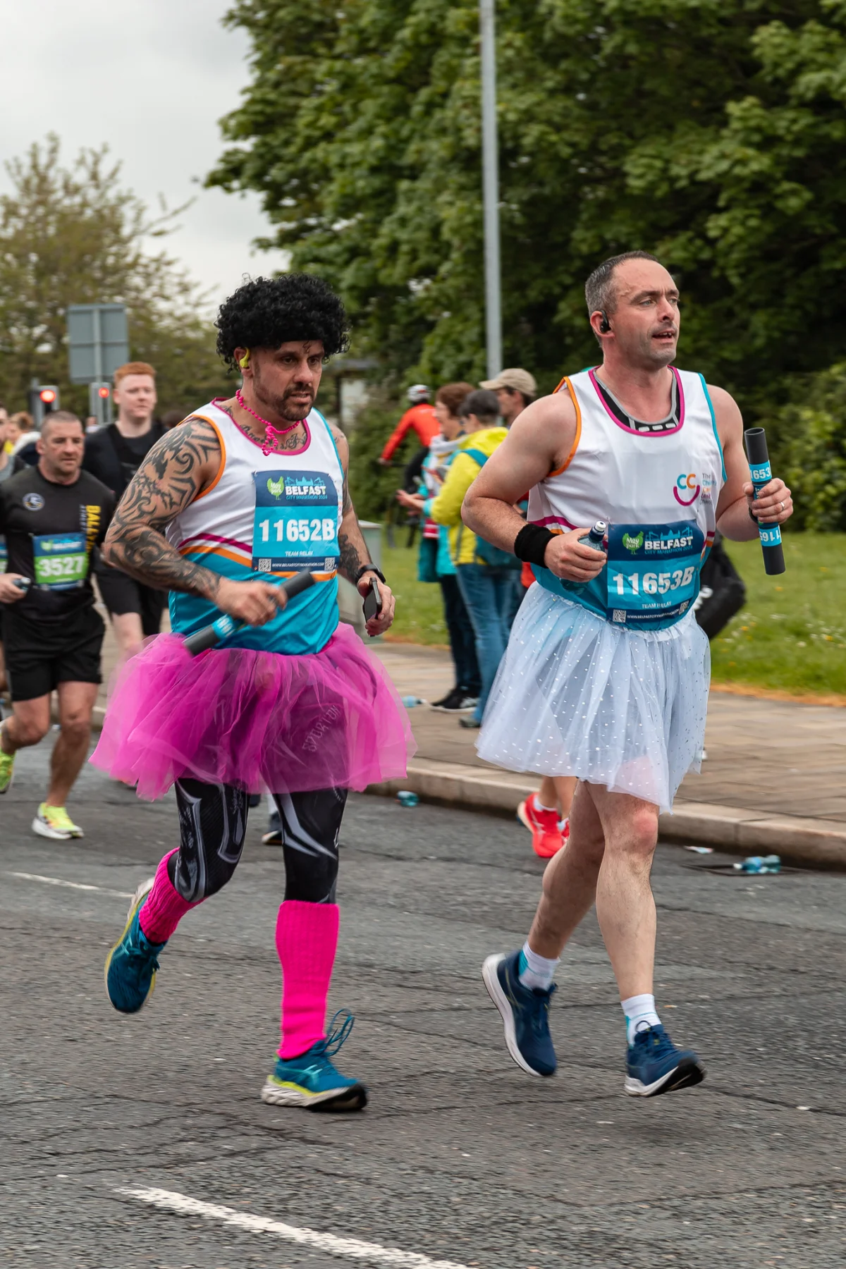 Two men in colorful tutus and running gear competing in an outdoor city race.