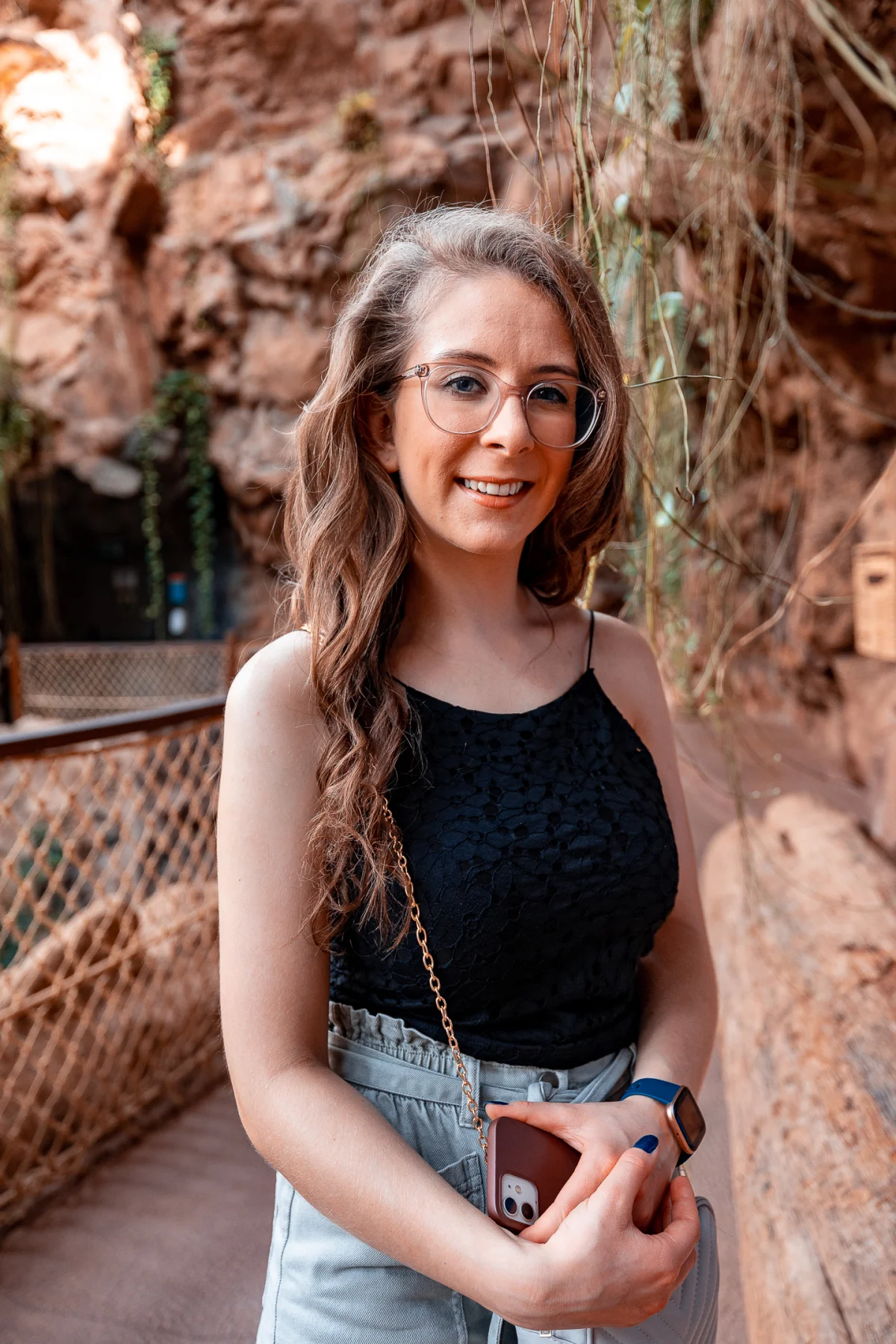 A smiling woman with glasses and long brown hair posing in front of a rocky cliff.
