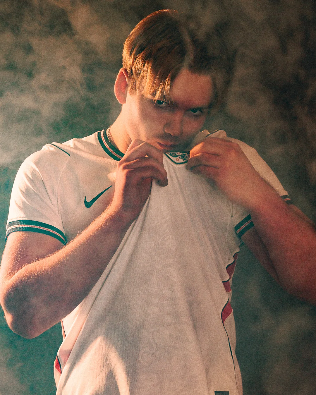Moody portrait of a young man in a white sports jersey surrounded by atmospheric smoke.