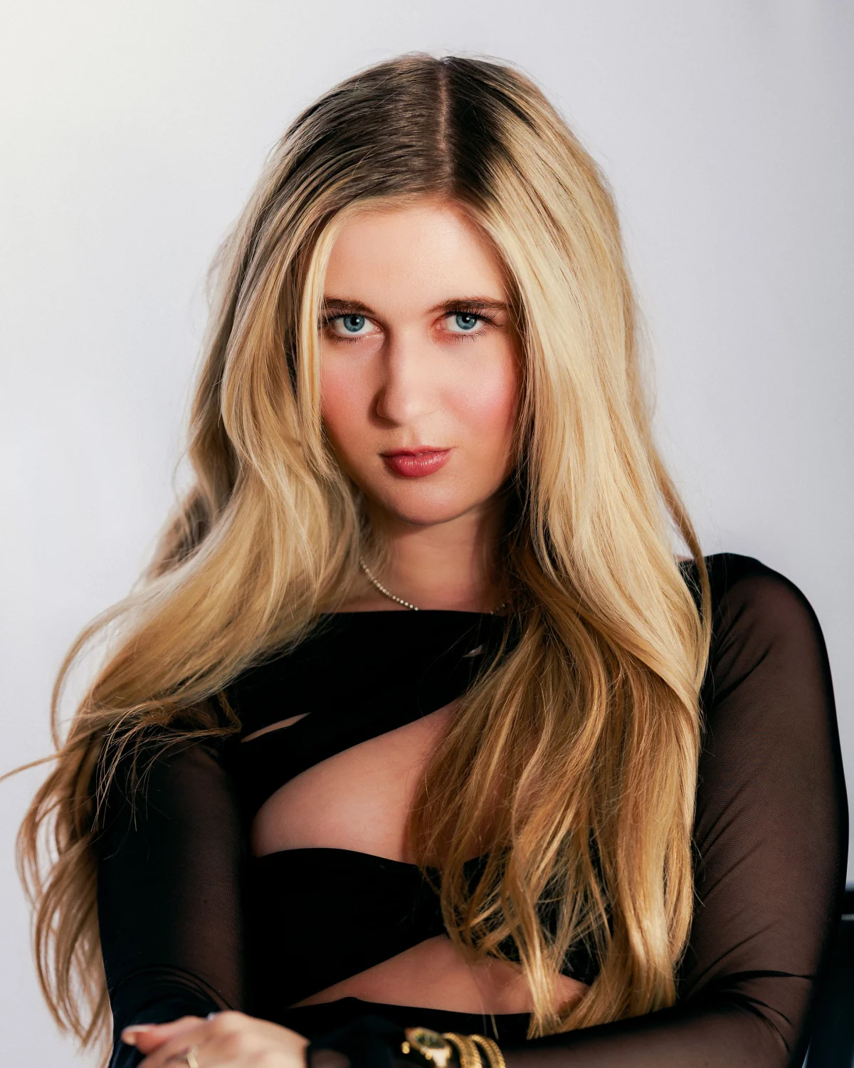 Close-up portrait of a blonde woman wearing a black cut-out dress against a light grey background.