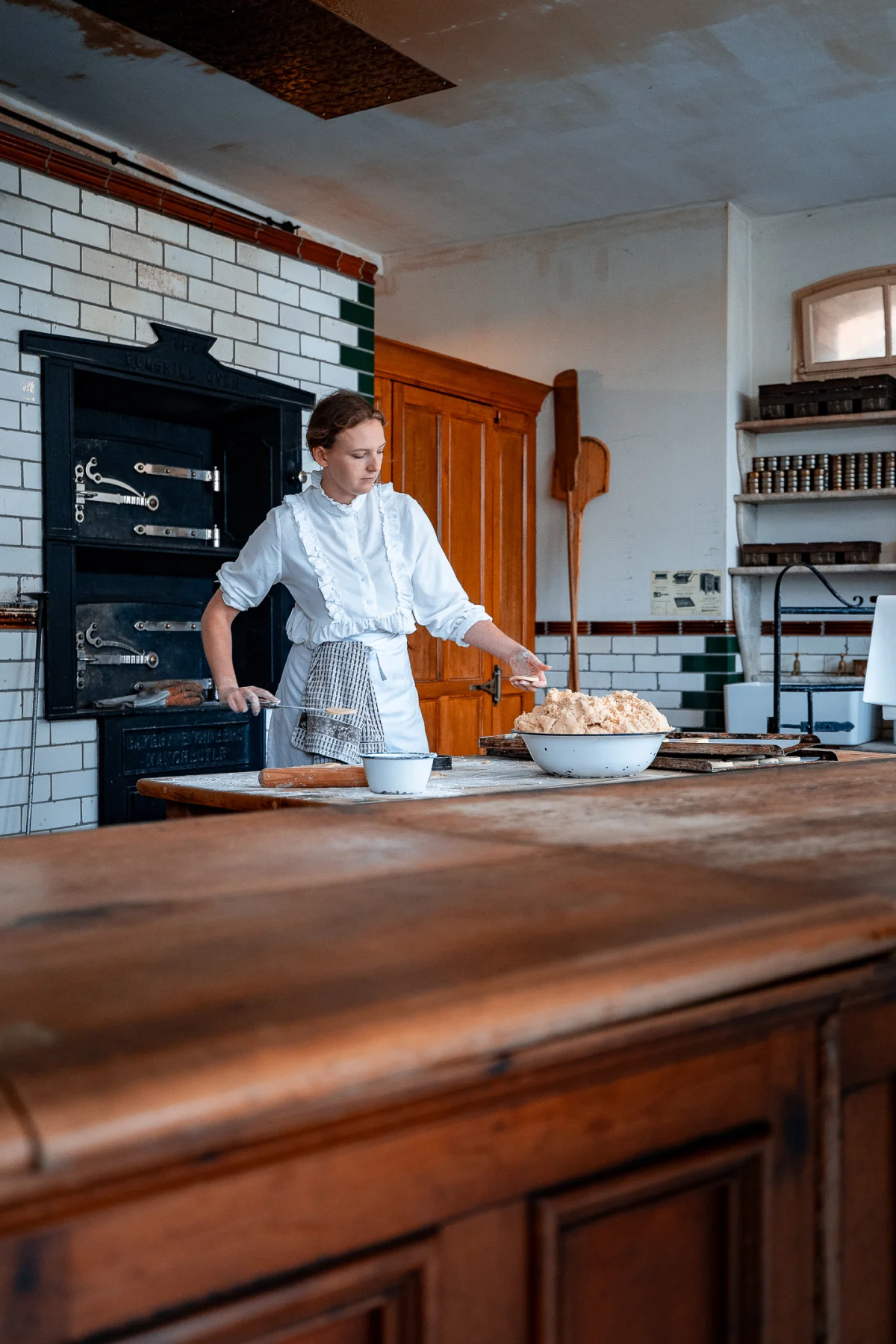 A woman in vintage white attire and apron baking bread in a rustic historical kitchen.