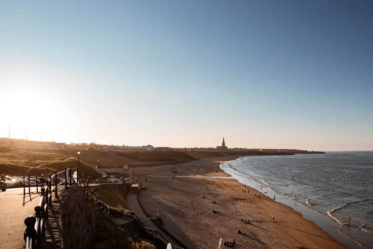 Wide shot of a sandy beach meeting the ocean at golden hour with a distant church spire.