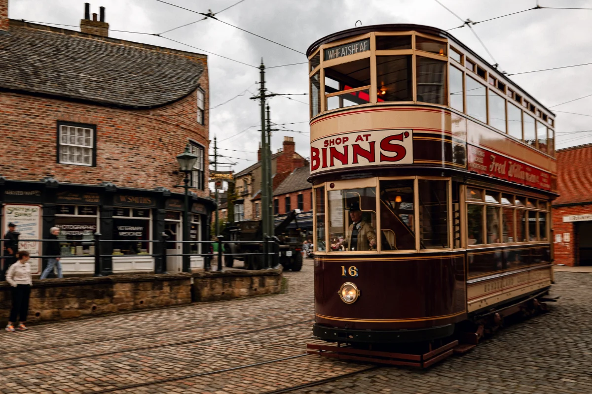 A vintage double-decker tram on a cobblestone street in a historic town setting.