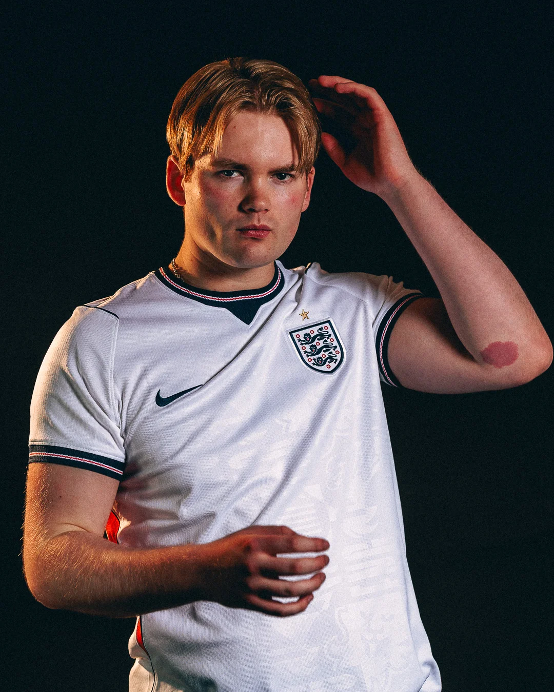 A young man in an England football jersey posing against a black background with studio lighting.