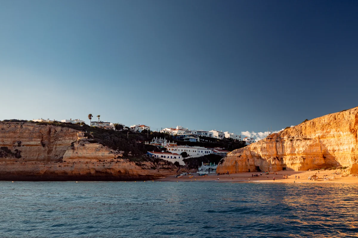 White houses perched on golden sandstone cliffs overlooking a sandy beach and blue ocean at sunset.