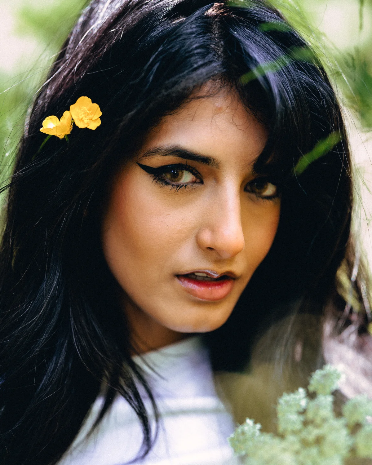 Close-up portrait of a woman with dark hair and yellow flowers in her hair against a soft green background.