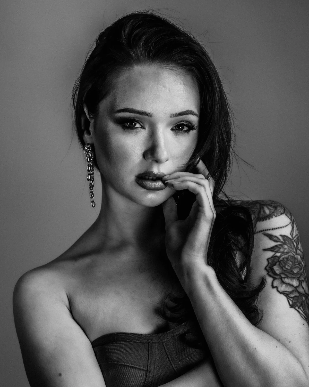 Black and white close-up portrait of a woman with dark hair and tattoos, posing thoughtfully.
