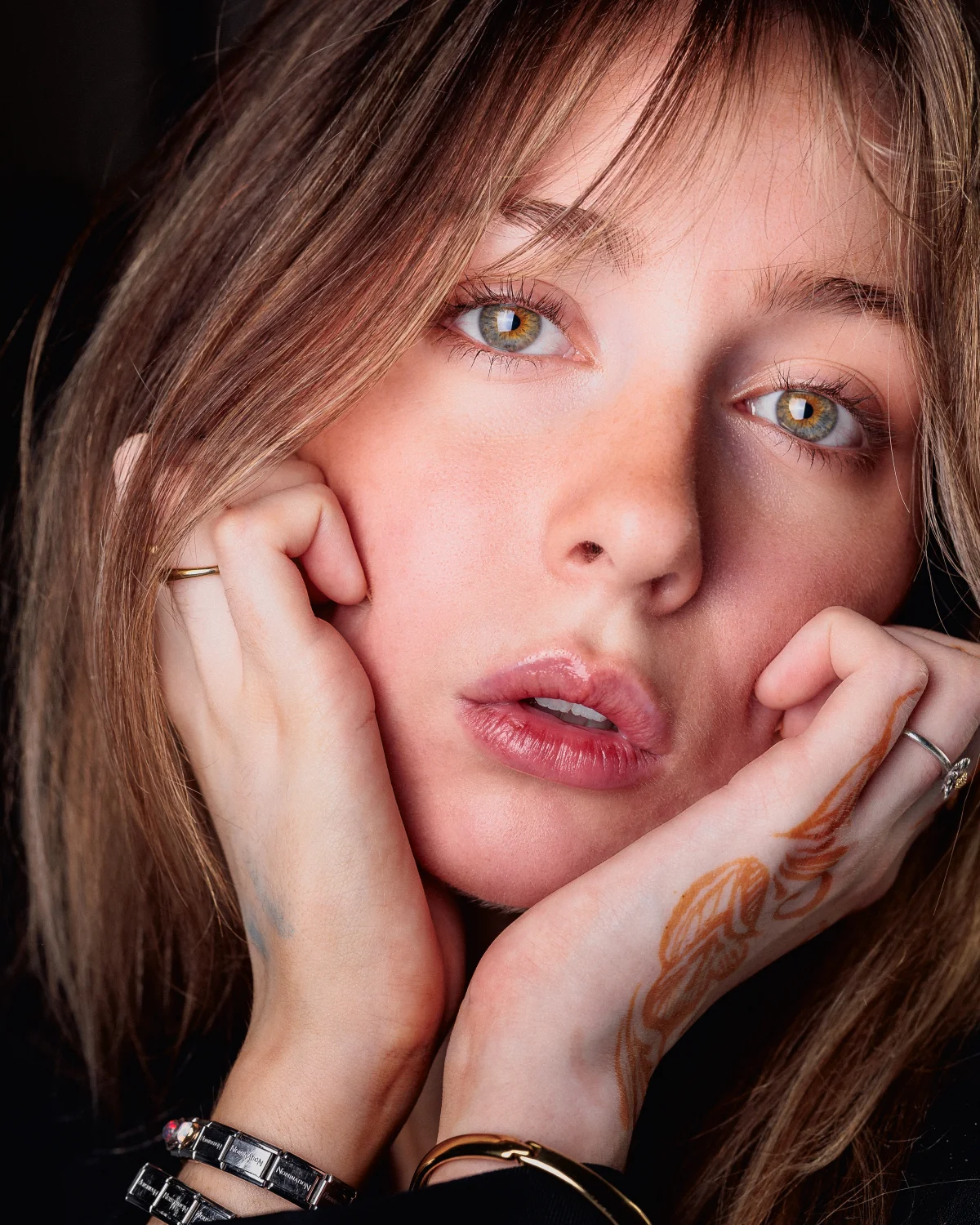 Close-up portrait of a young woman with light eyes resting her chin on her hands.