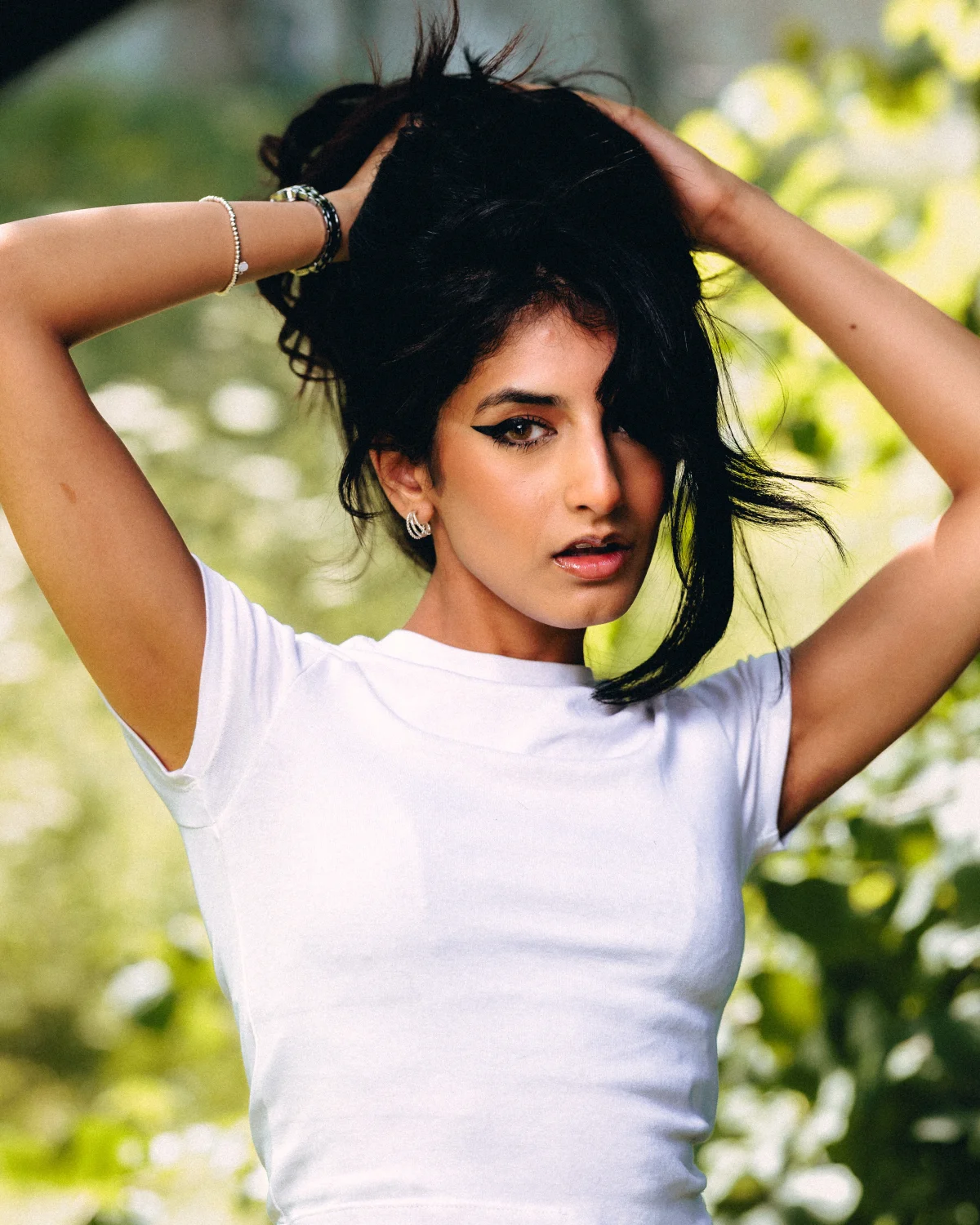 Portrait of a woman with dark hair and winged eyeliner posing outdoors in a white t-shirt.