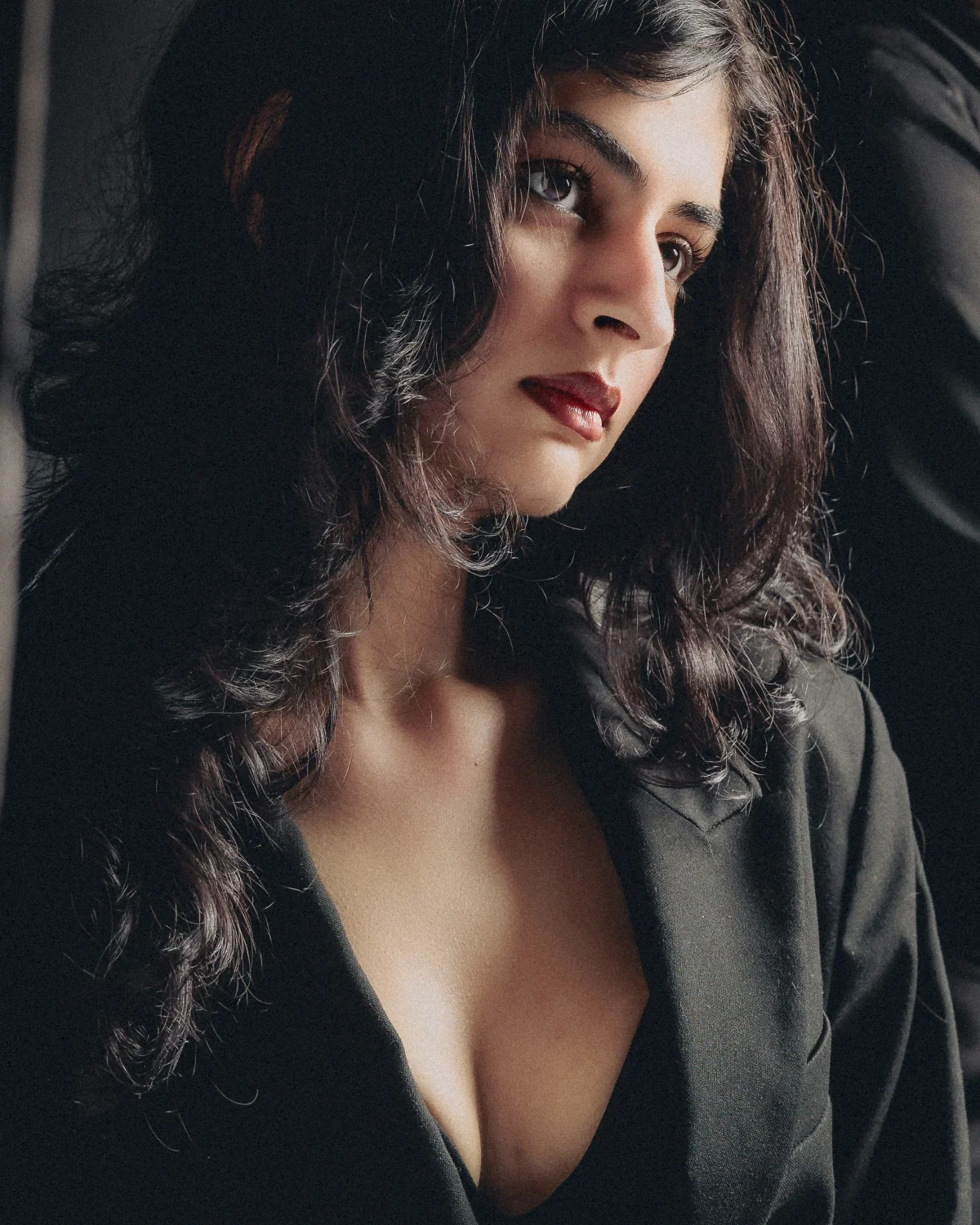 Moody close-up portrait of a woman with dark hair and red lipstick wearing a black blazer.