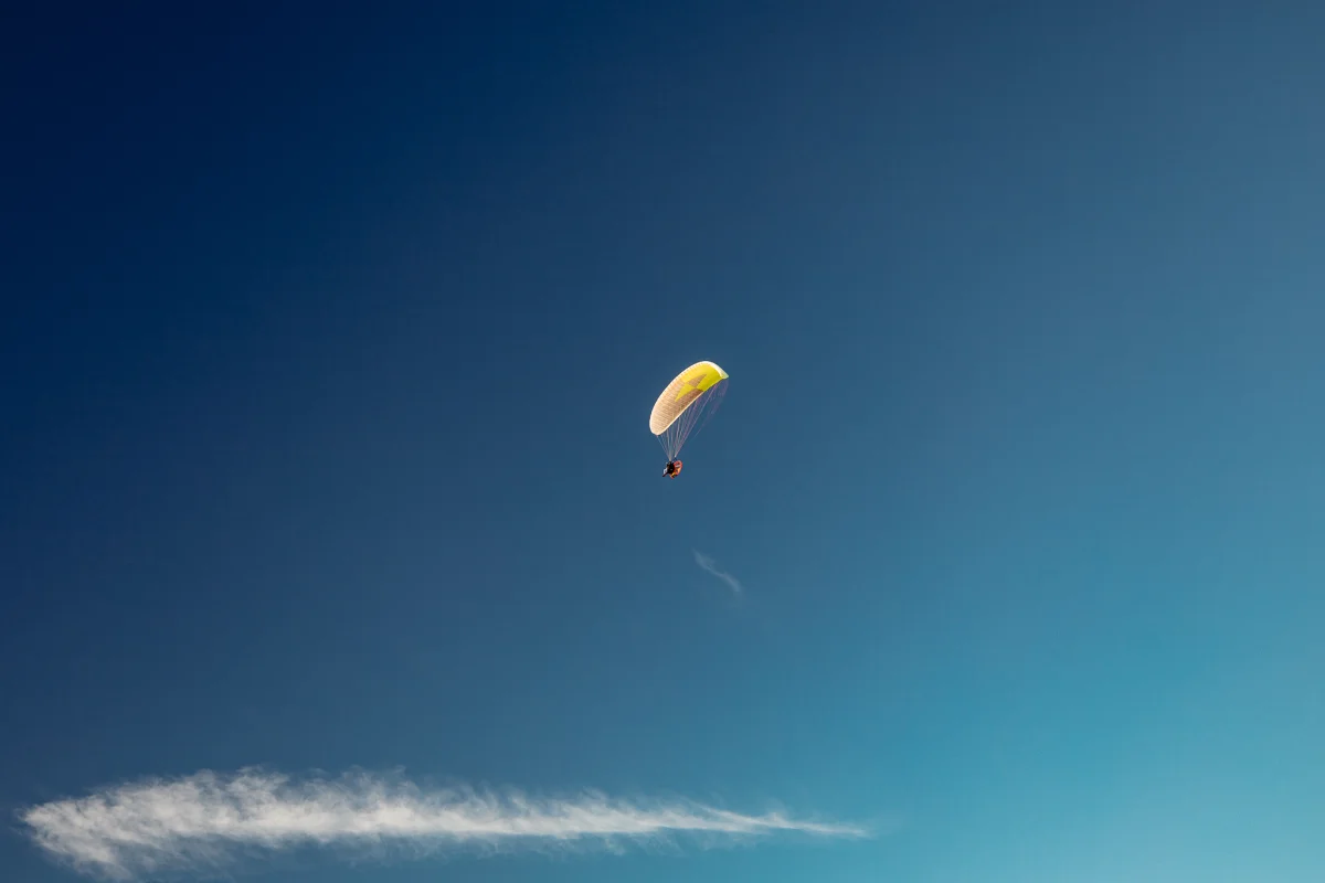 A person paragliding with a yellow parachute against a vast, clear blue sky.