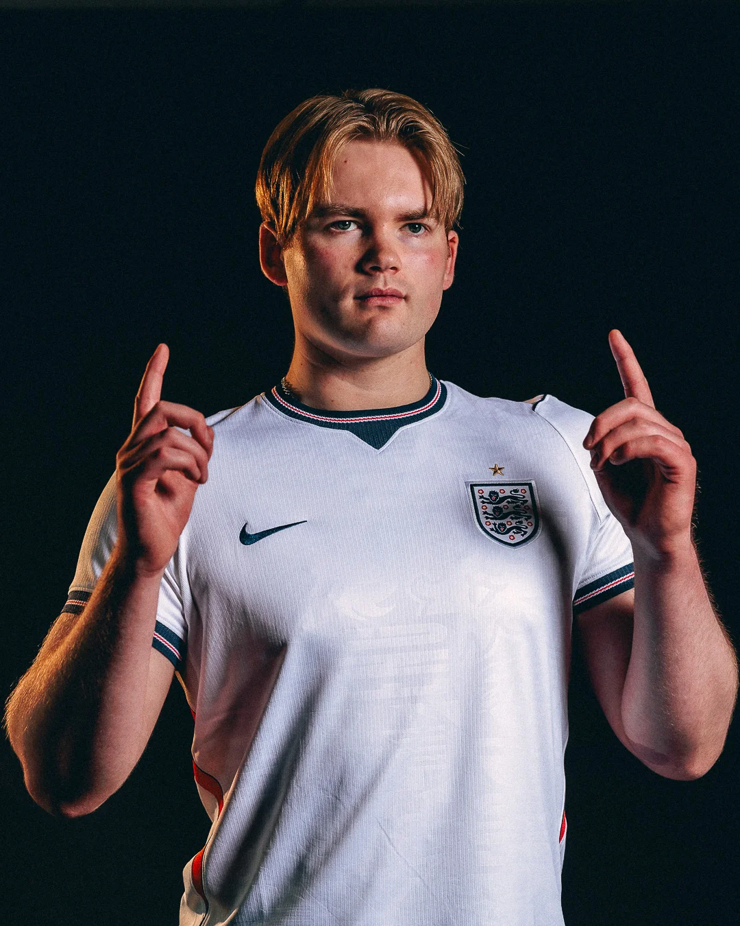 Studio portrait of a young man in an England football jersey posing against a black background.
