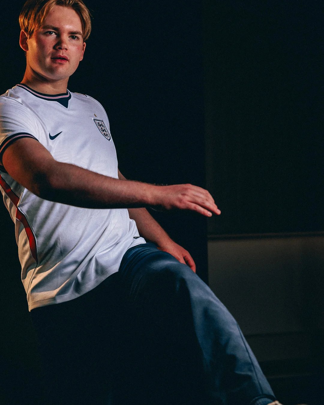 A young man in a white England football jersey posing with dramatic studio lighting against a dark background.
