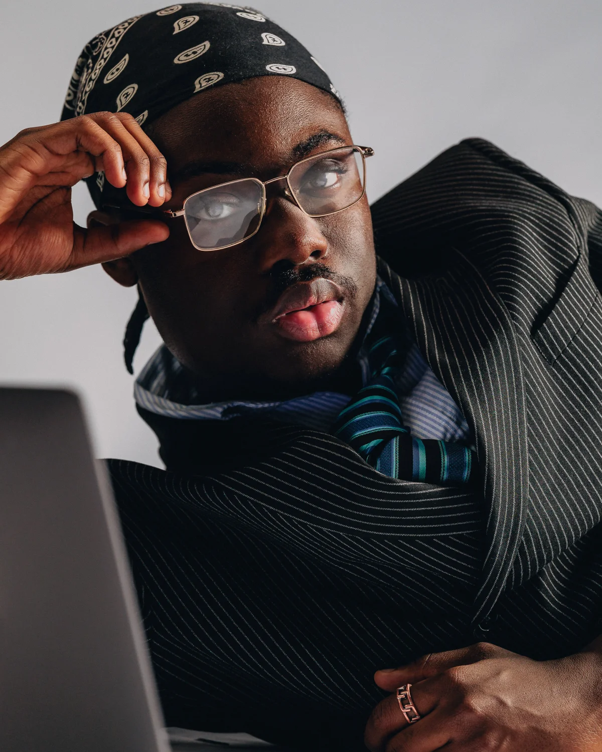 A man in a black bandana and pinstripe suit looks thoughtfully at a laptop screen.