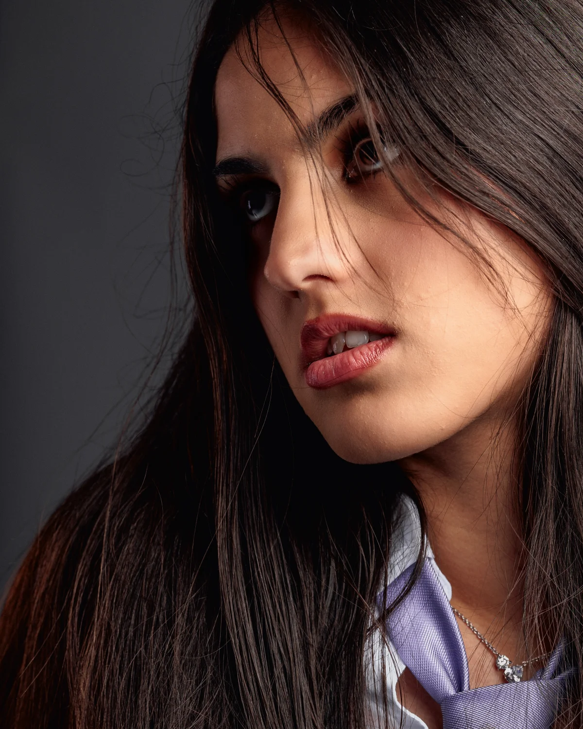 Close-up portrait of a woman with long dark hair and a thoughtful expression against a neutral grey background.