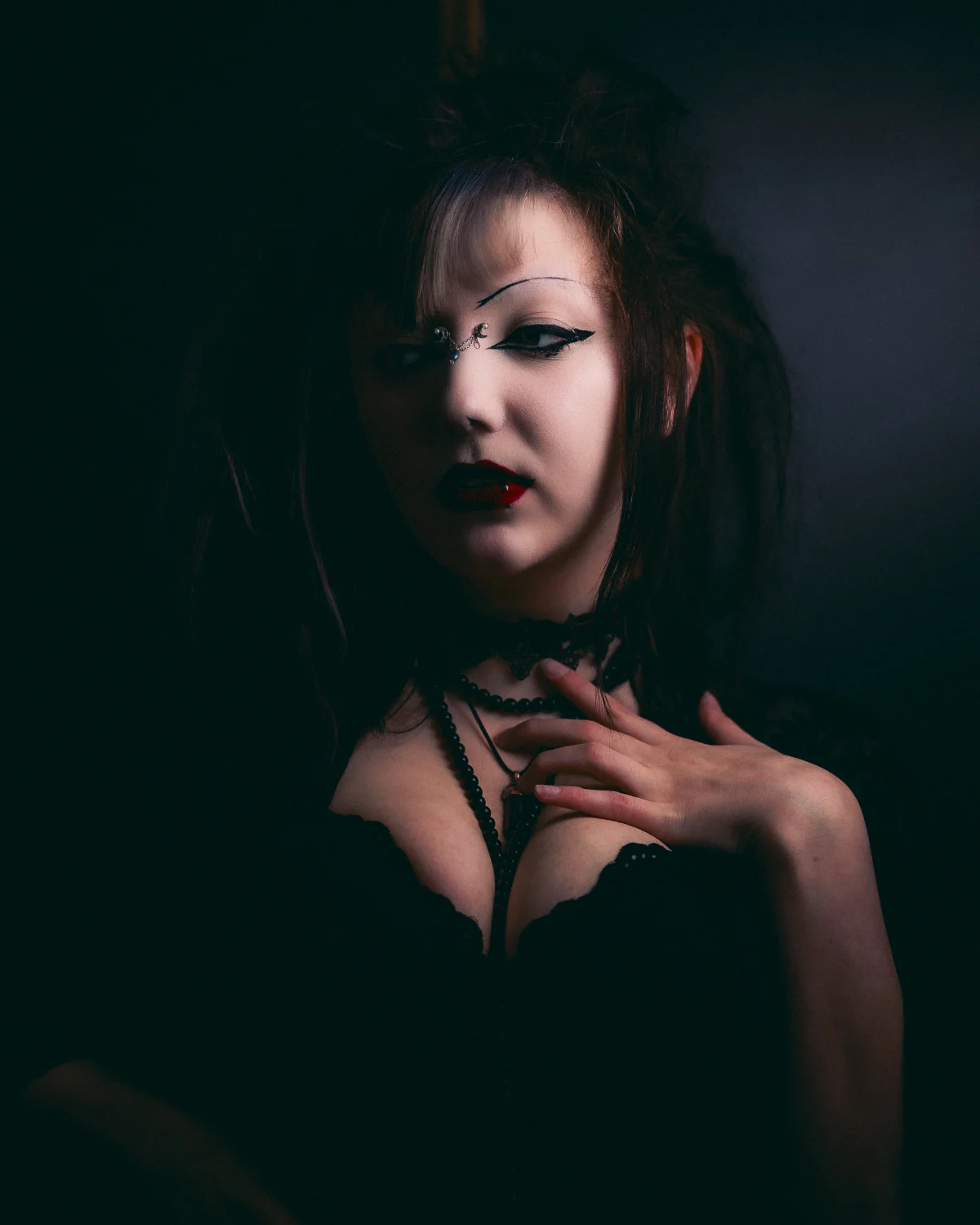A woman with gothic makeup and dark red lipstick posing against a dark background in a moody portrait.