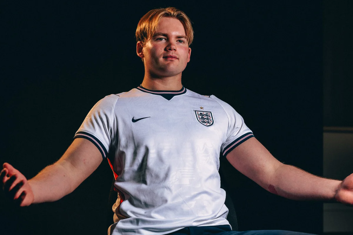 Young man in an England football jersey posing against a dark background with dramatic lighting.