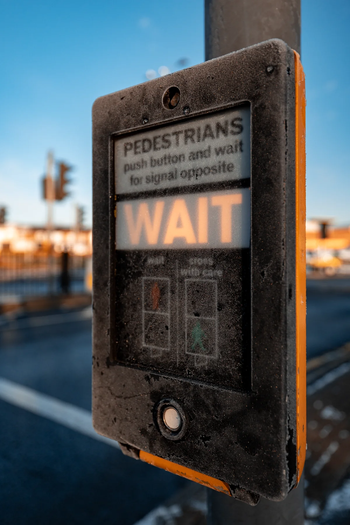 Close-up of a weathered pedestrian crossing signal displaying a glowing orange 'WAIT' sign on an urban street.