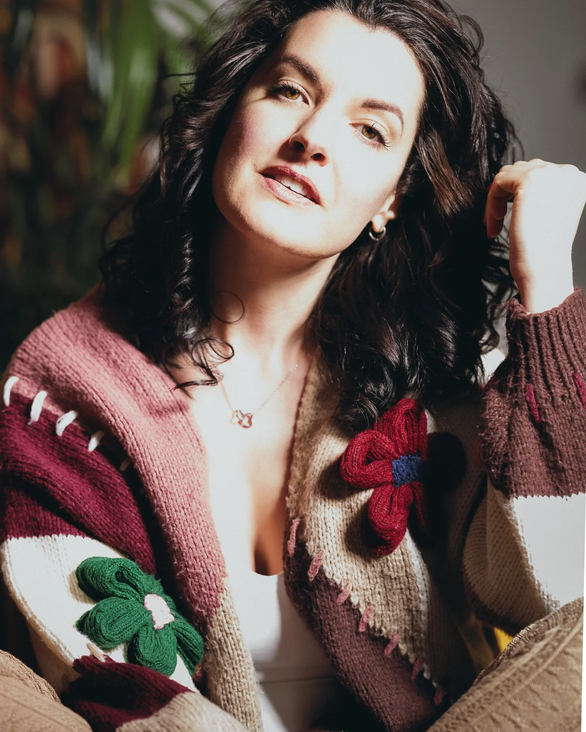Close-up portrait of a woman with dark curly hair wearing a colorful knitted flower cardigan.