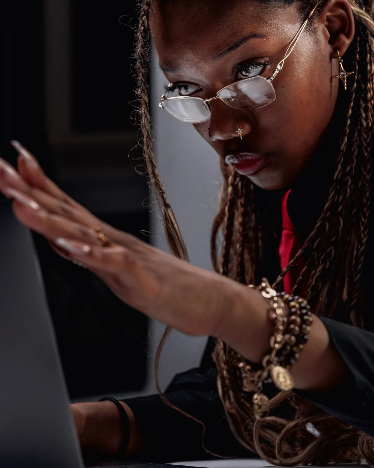 Close-up portrait of a Black woman with braids and glasses looking intently at a screen.