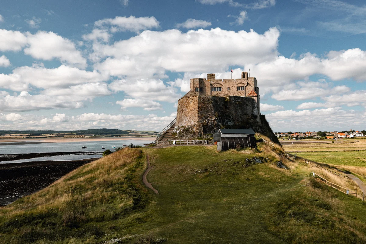 Historic stone castle atop a rocky hill overlooking a coastal landscape under a cloudy blue sky.