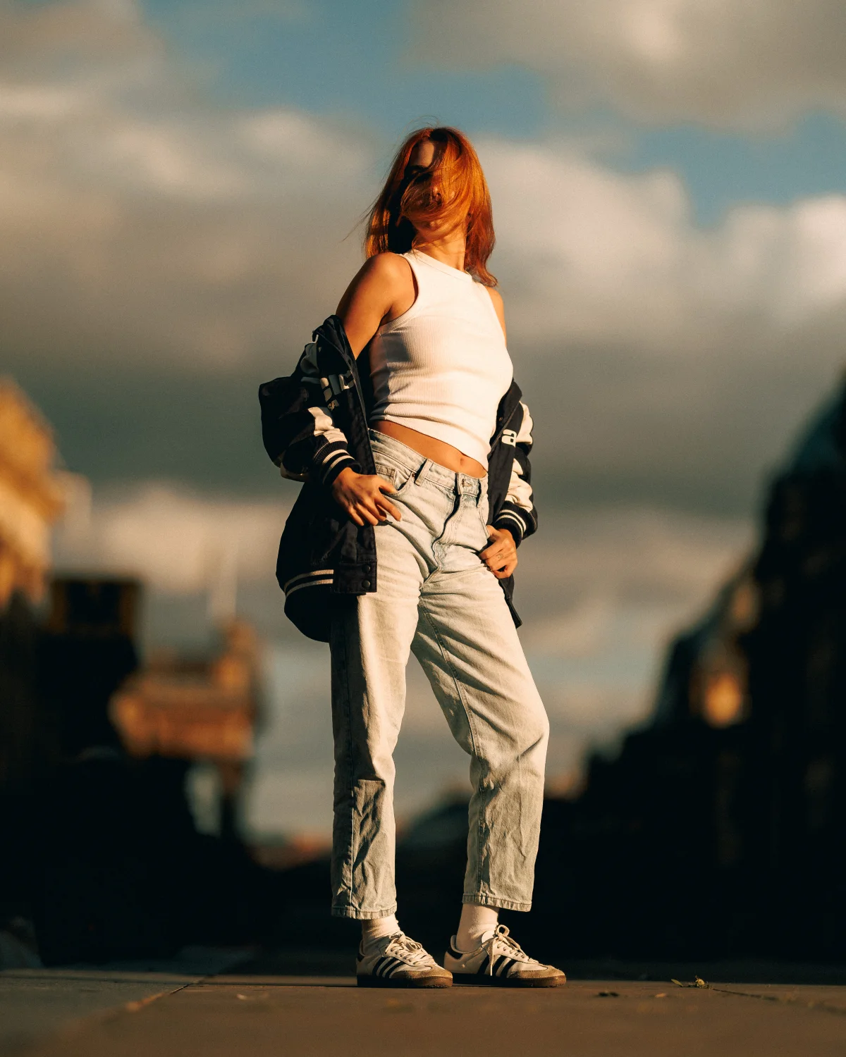 Full-body shot of a red-haired woman in a white crop top and light-wash jeans standing outdoors during golden hour.