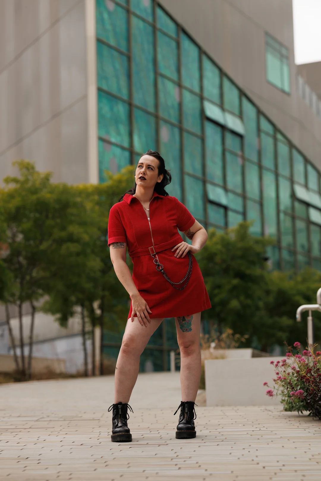 A woman in a red mini dress and black boots posing confidently in front of a modern glass building.