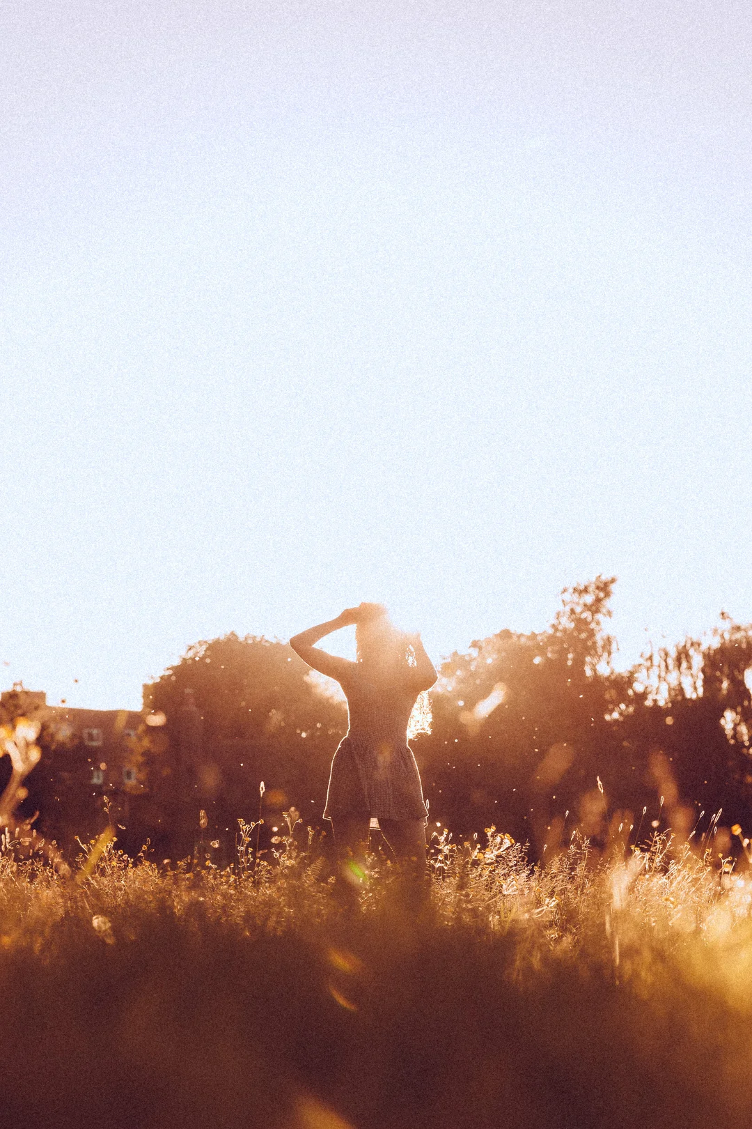 Silhouette of a woman standing in a golden field at sunset, backlit by warm sunlight.
