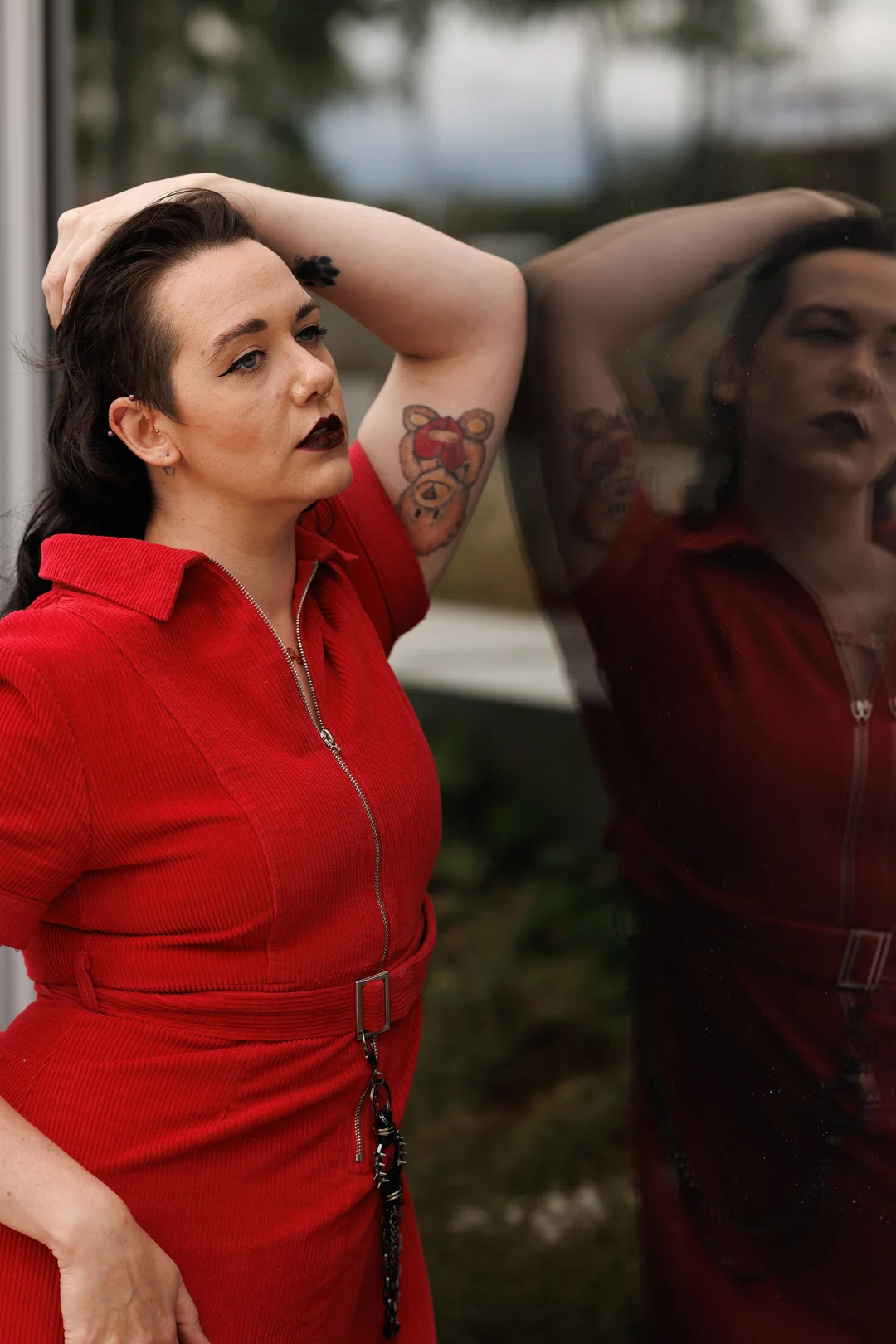 Portrait of a person in a red corduroy dress posing against a reflective glass surface.