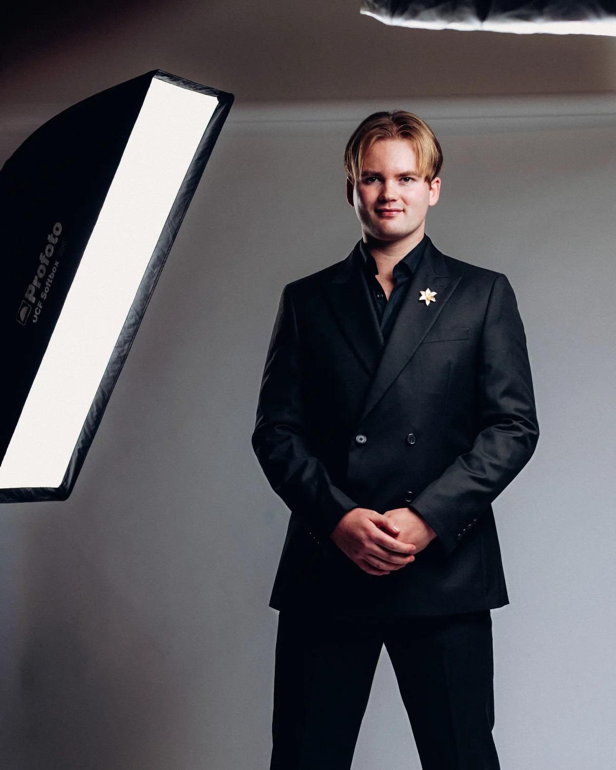 A man in a black double-breasted suit posing in a studio with professional lighting equipment visible.