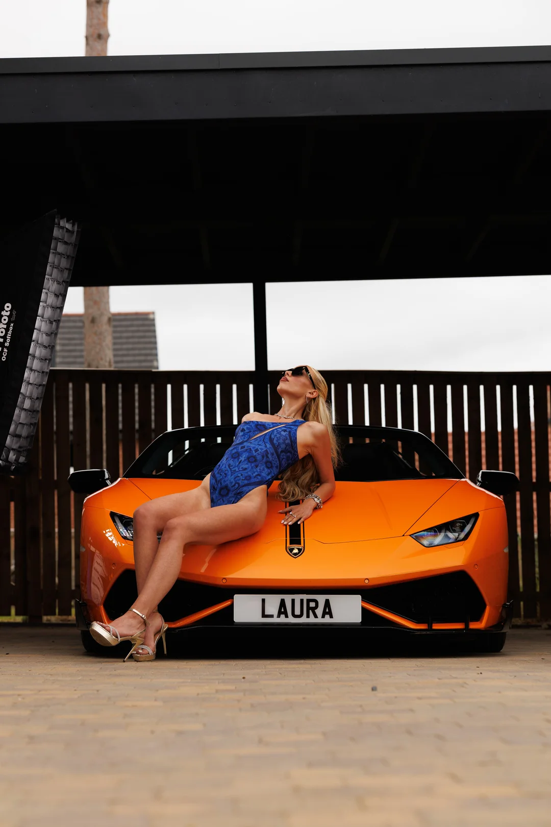 A woman in a blue swimsuit posing on the hood of an orange luxury sports car.