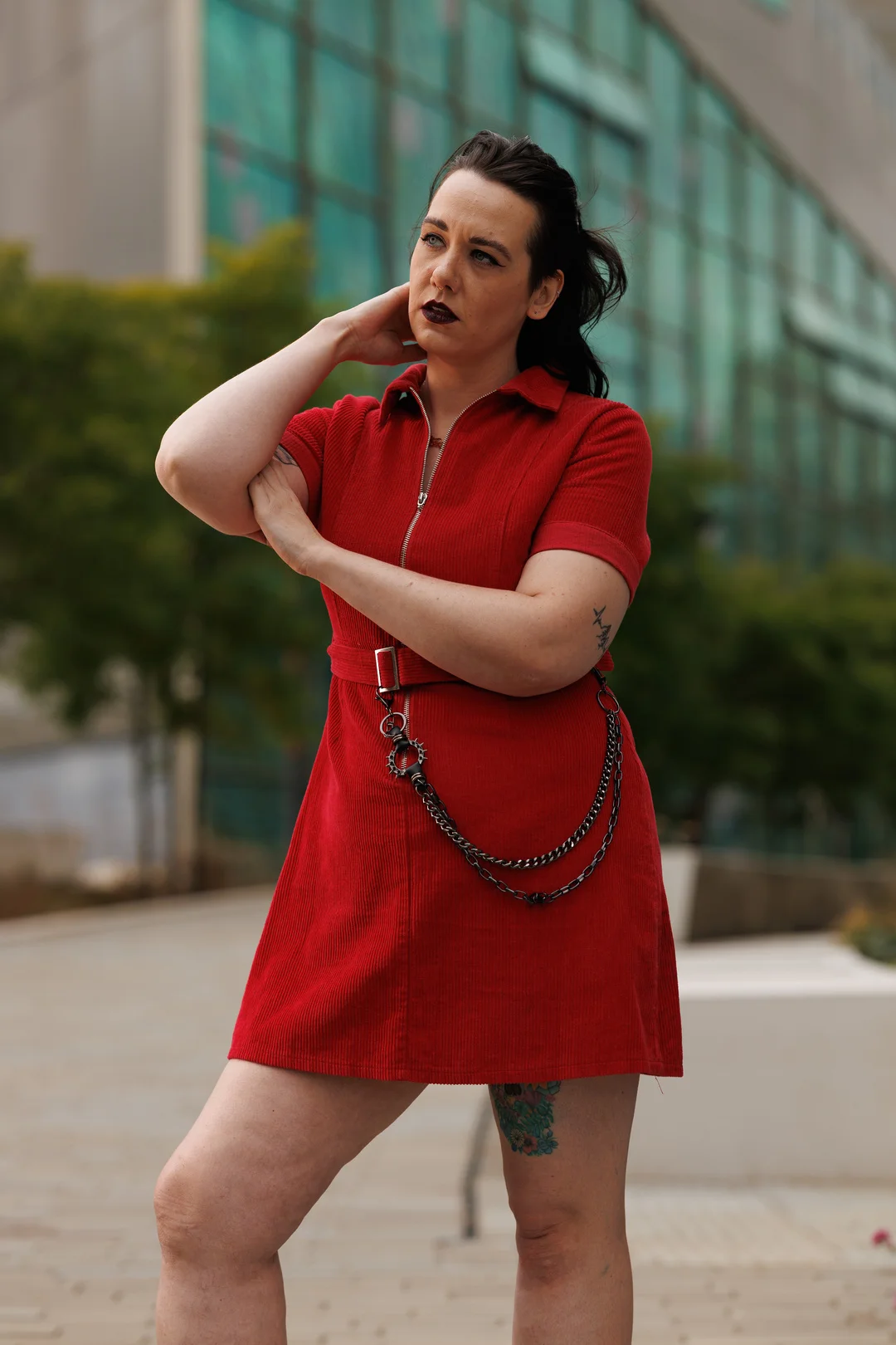 A woman in a red corduroy dress posing outdoors in front of a modern glass building.