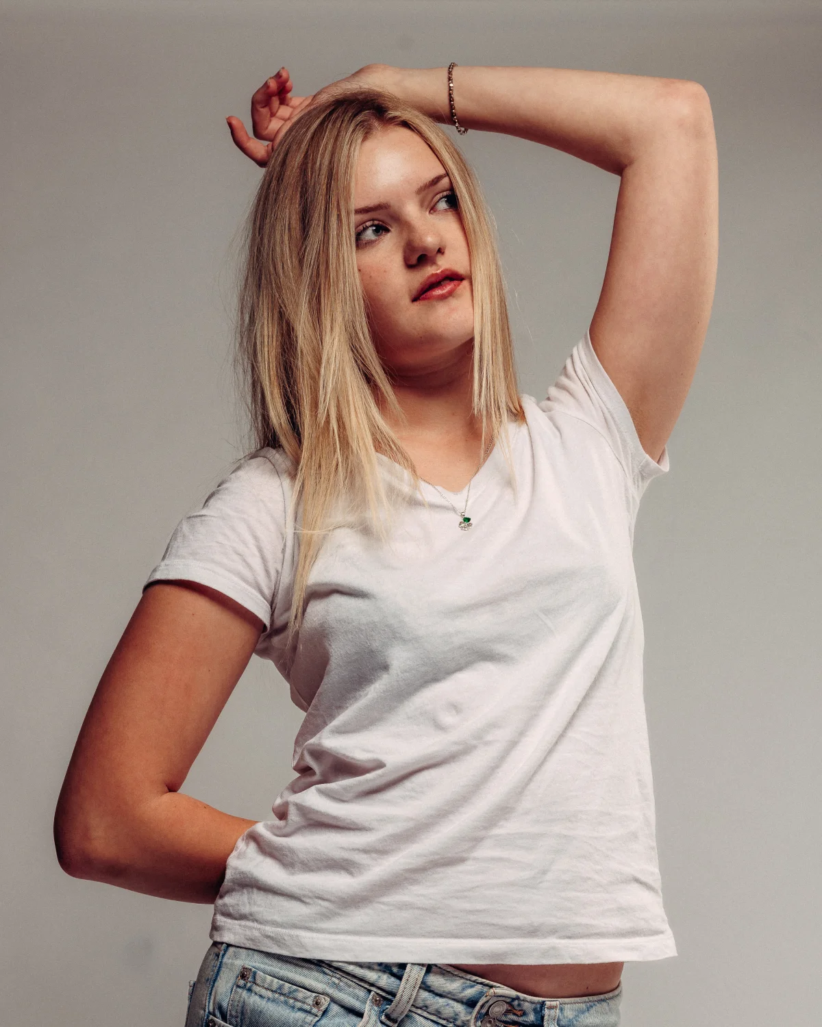Young woman with blonde hair in a white t-shirt posing against a neutral grey studio background.