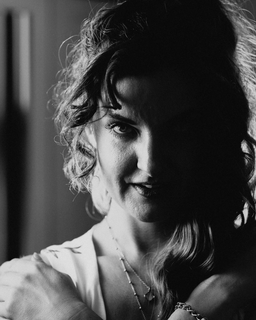 Moody black and white close-up portrait of a woman with curly hair, partially in shadow.