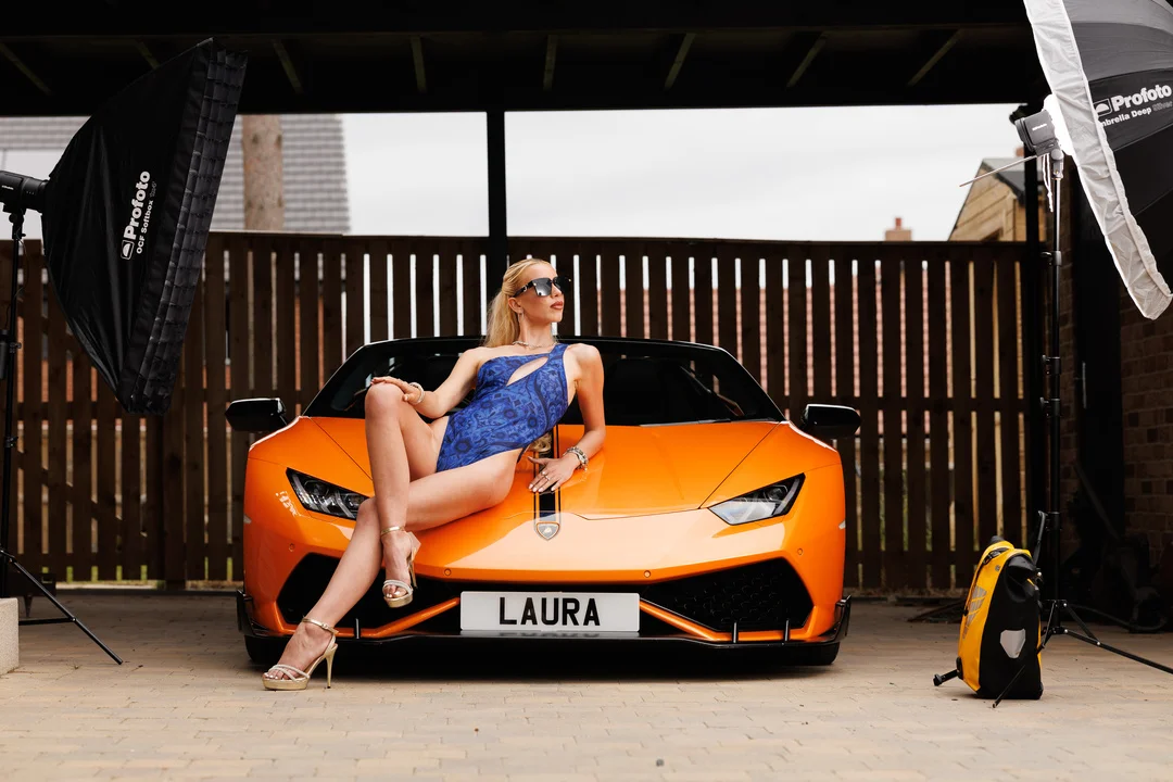 Woman in a blue dress posing on an orange Lamborghini with professional studio lighting outdoors.